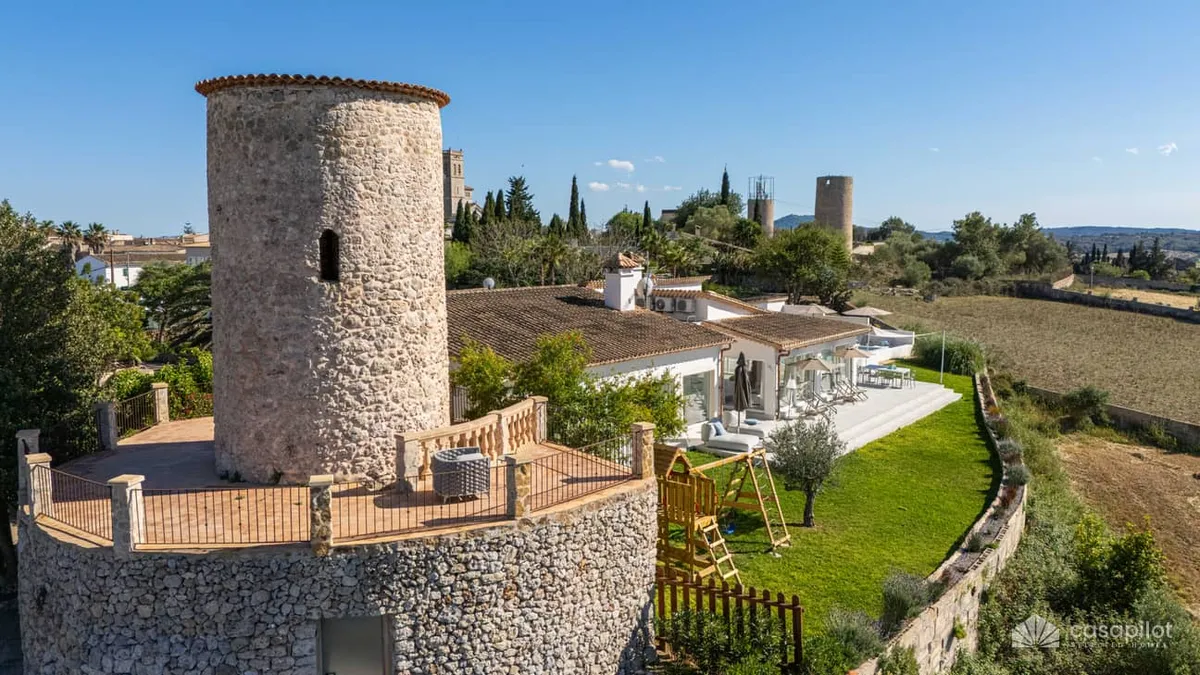 Aerial view of a renovated stone tower and modern house in sunny Arinay, Spain.