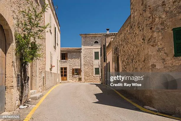 A charming, narrow street lined with traditional stone buildings under blue skies in Costitx, Mallorca, Spain.