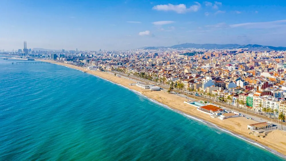 Aerial view of Badalona's beautiful Mediterranean coastline, sandy beaches, and bustling cityscape under a blue sky.