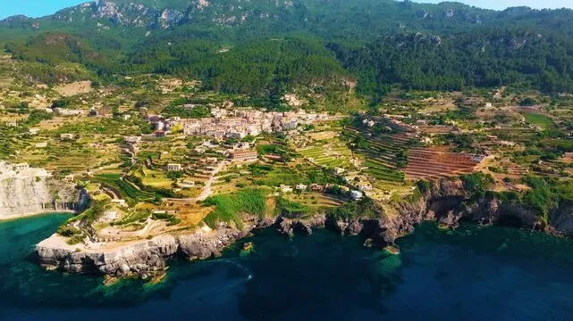 Aerial view of coastal Banyalbufar, Spain, showing cliffside town and terraces. Buycannabisbanyalbufar Buyweedbanyalbufar.