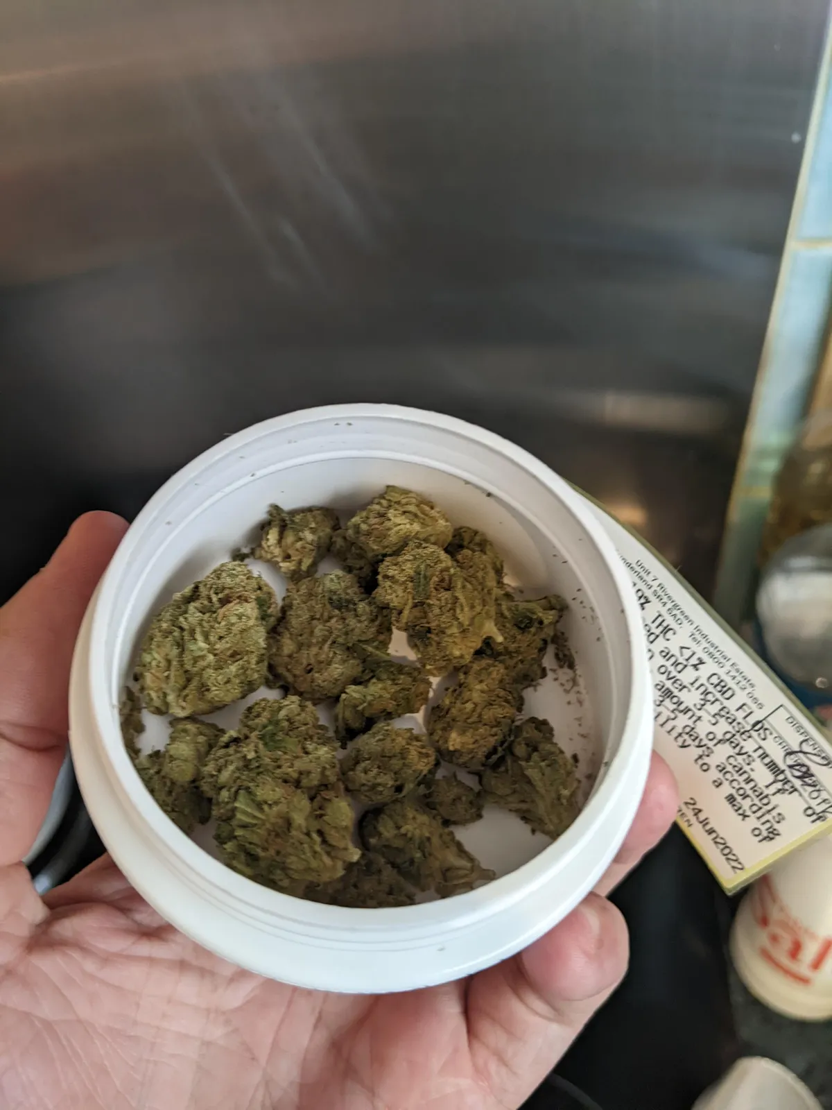 Hand holding an open container of green cannabis buds from a Ronda social club.